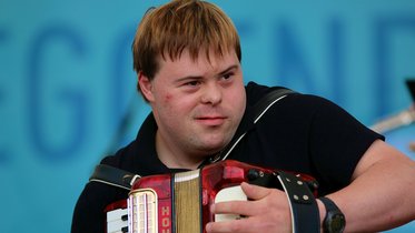 Junger Mann mit Downsyndrom spielt Akkordeon
