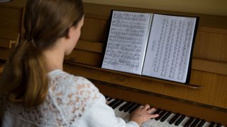 jugendliches Mädchen spielt Klavier, die Kamera blickt über ihre Schulter auf die Noten