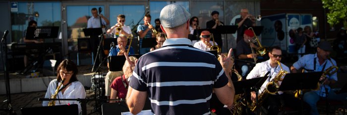 Big Band bei einem Open Air Konzert, im Zentrum der Dirigent von hinten 