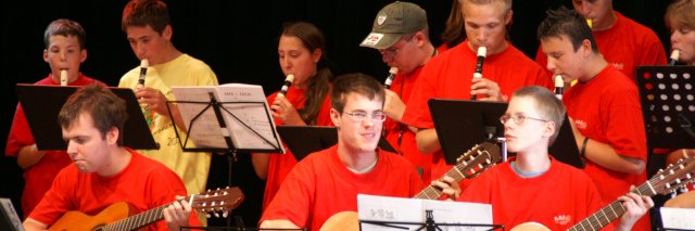Mehrere Musiker:innen mit Blockflöten und Gitarren in roten T-Shirts auf der Bühne