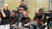Musiker:innen mit Behinderung auf der Open Air Bühne. Im Vordergrund eine Sängerin, dahinter mehrere Menschen mit diversen Percussioninstrumenten und Schlagzeugestival der Musikschule Fürth