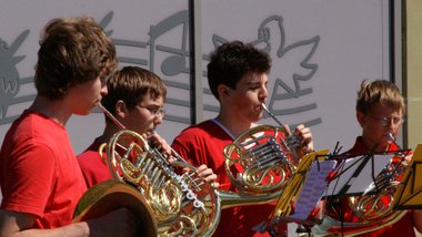 Jugendliche in roten T-Shirts spielen Horn