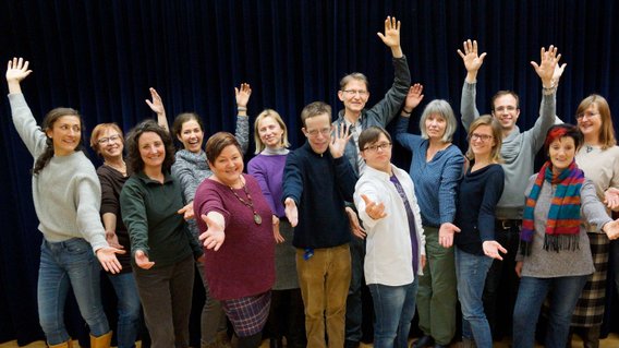Die Mitglieder des Wellness-Chores posieren mit ausgestreckten Armen für ein Gruppenbild