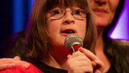 Mädchen singt auf der Bühne, eine Frau legt ihr einen Arm um die Schulter