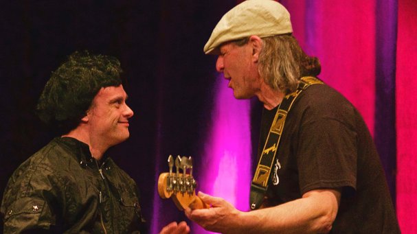Zwei Männer rocken gemeinsam. Der eine spielt E-Gitarre, der andere trägt eine schwarze Lockenperücke