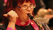 Eine junge Frau mit Down-Syndrom spielt Saxofon und streckt den rechten Daumen in die Luft