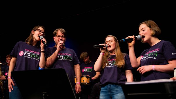 ein Sänger und drei Sängerinnen mit Mikros, alle tragen das Festival-T-Shirt FIS 2019