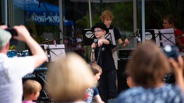 Kinderband bei Auftritt im Freien, im Vodergrund die Köpfe des Publikums von hinten