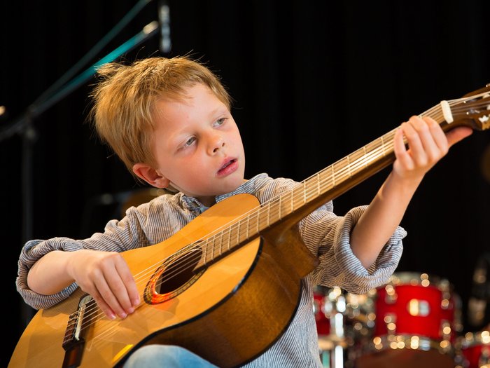 Junge spielt Gitarre und schaut konzentriert auf das Griffbrett