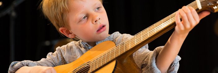 Junge spielt Gitarre und schaut konzentriert auf das Griffbrett