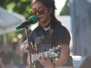 Junge Frau in rockiger Kleidung spielt E-Gitarre bei einem Open-Air-Konzert