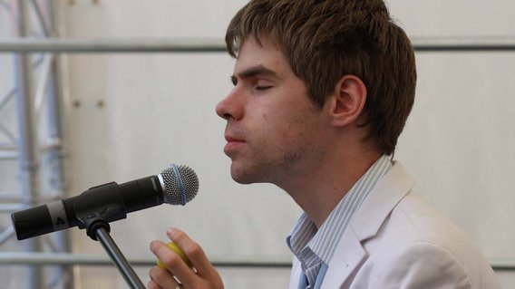 Ein blinder junger Mann singt, vor ihm steht ein Mikro