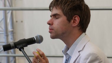 Ein blinder junger Mann singt, vor ihm steht ein Mikro