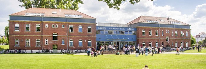 Gebäude der Musikschule Fürth im Südstadtpark, davor viele Menschen in der Sonne