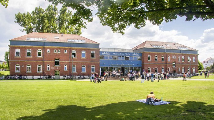 Gebäude der Musikschule Fürth im Südstadtpark, davor viele Menschen in der Sonne
