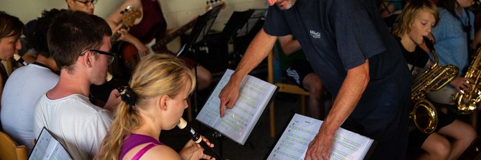 Jugendliche spielen Blockflöte, vor sich Notenständern mit in Buchstaben notierter Musik.