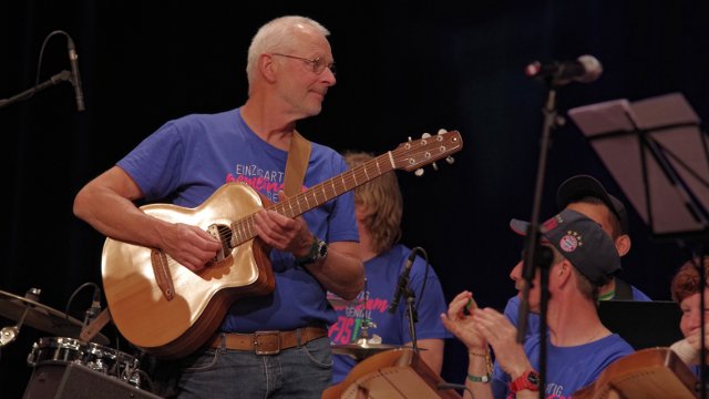Älterer Gitarrist mit weißem Haar, er trägt das Festival-T-Shirt