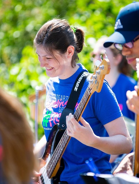 zwei jugendliche, Junge und Mädchen, lächelnd mit E-Bass bei Open-Air-Auftritt