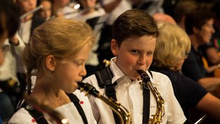 Junge und Mädchen im Schulalter spielen Saxofon, der junge zwinkert frech in die Kamera