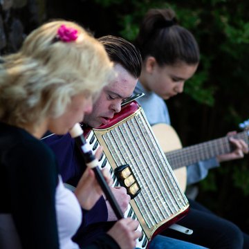 Jugendliche machen Musik zusammen, 2 Mädchen mit Blockflöte und Gitarre, Junge mit Down-syndrom spielt Akkordeon
