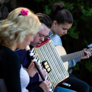 Jugendliche sitzen auf Bank im Freie und musizieren zusammen mit Blockflöte, Akkordeon und Gitarre