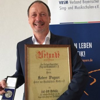 Robert Wagner freudig mit Carl-Orff-Medaille und dazugehöriger Urkunde in den Händen