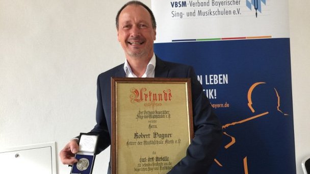 Robert Wagner freudig mit Carl-Orff-Medaille und dazugehöriger Urkunde in den Händen