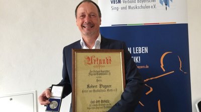 Robert Wagner freudig mit Carl-Orff-Medaille und dazugehöriger Urkunde in den Händen