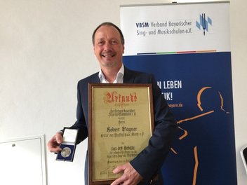 Robert Wagner freudig mit Carl-Orff-Medaille und dazugehöriger Urkunde in den Händen