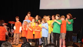 Kinderchor in bunten T-Shirts singt und gestikuliert