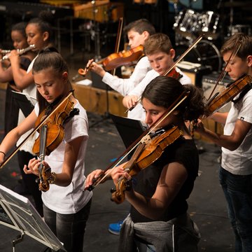 Jugendliche spielen Geige, sie tragen weiße T-Shirts und stehen auf einer Bühne