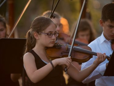 Mädchen spielt bei einem Open-Air Konzert Violine, im Hinterrgund weitere Orchestermitglieder