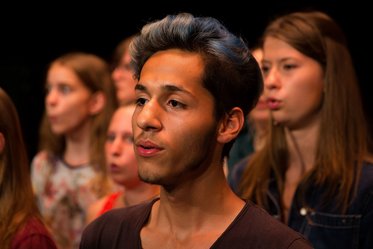 Jugendliche singen im Chor, im Vordergrund ein junger Mann