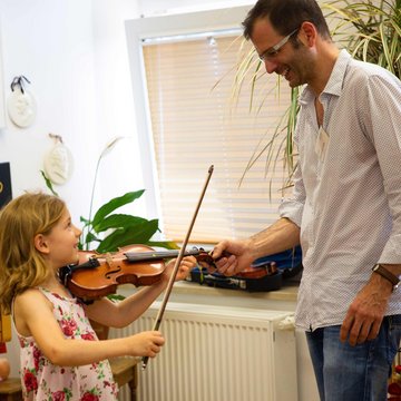 Lehrer und junges Mädchen mit Geige im Unterricht, lachen miteinander