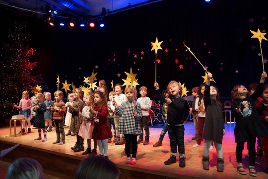 Viele Kindergartenkinder stehen auf der Bühne und halten gelbe gebastelte Papiersterne in die Höhe