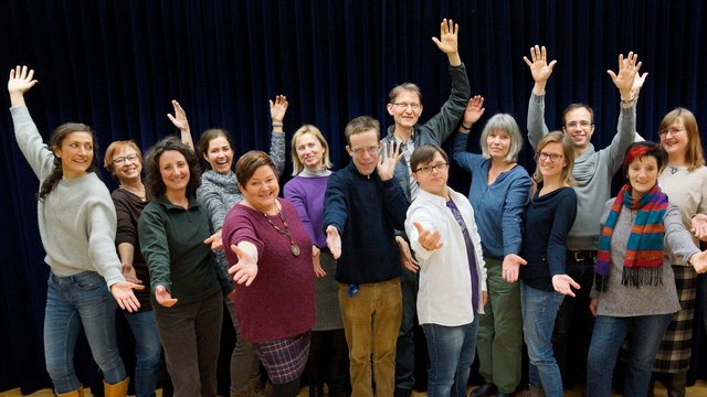 Die Mitglieder des Wellness-Chores posieren mit ausgestreckten Armen für ein Gruppenfoto