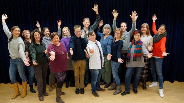 Die Mitglieder des Wellness-Chores posieren mit ausgestreckten Armen für ein Gruppenfoto