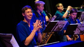 Pianist klatscht sich lachend in die Hände, im Hintergrund Saxofon-Kinder