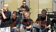 Musiker:innen mit Behinderung auf der Open Air Bühne. Im Vordergrund eine Sängerin, dahinter mehrere Menschen mit diversen Percussioninstrumenten und Schlagzeugestival der Musikschule Fürth