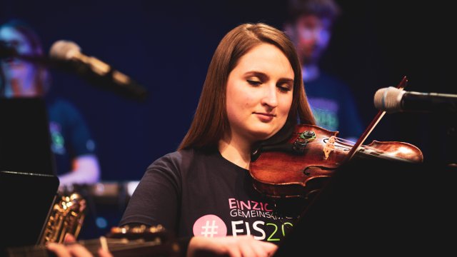 Junge Frau spielt Geige, sie trägt das Festival-T-Shirt FIS 2019