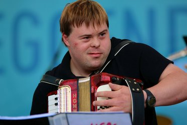 Junger Mann mit Downsyndrom spielt Akkordeon