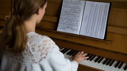 Mädchen am Klavier, die Kamera schaut ihr über den Rücken