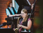 Junge Frau spielt Saxofon, im Hintergrund ist eine Pianistin zu sehen