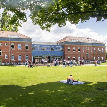 Das Musikschulgebäude im Südstadtpark, davor viele Menschen in der Sonne