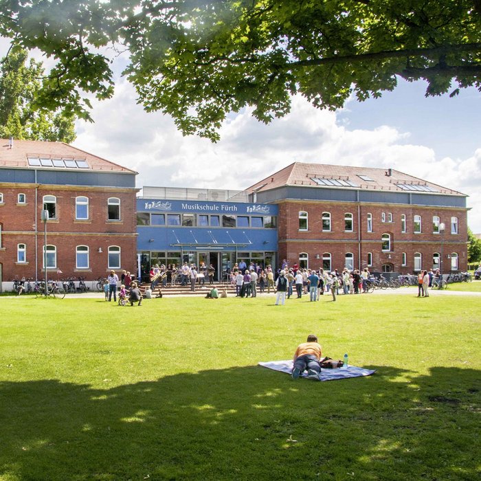 Gebäude der Musikschule Fürth im Südstadtpark, davor viele Menschen im Sonnenschein 