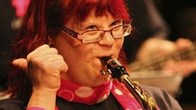 Eine junge Frau mit Down-Syndrom spielt Saxofon und streckt den rechten Daumen in die Luft