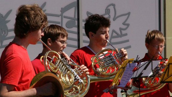 Jugendliche in roten T-Shirts spielen Horn