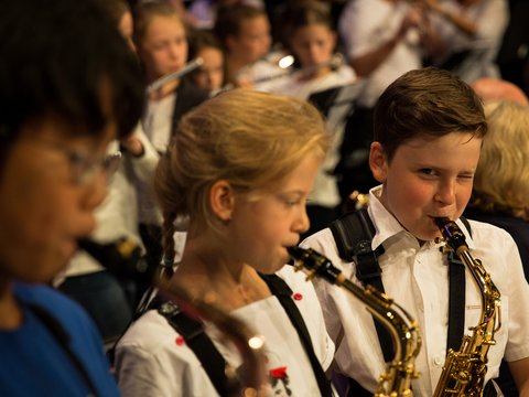 Kinder spielen Saxofon, ein Junge zwinkert in die Kamera