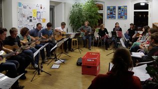 Jugendliche und Erwachsenen sitzen im Kreis, einige spielen Gitarre, andere singen