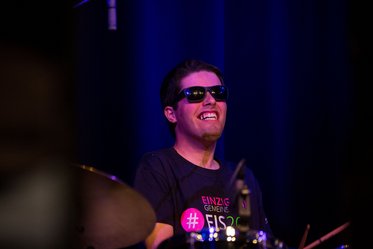 junger Mann mit Sonnenbrille und breitem Grinsen am Schlagzeug